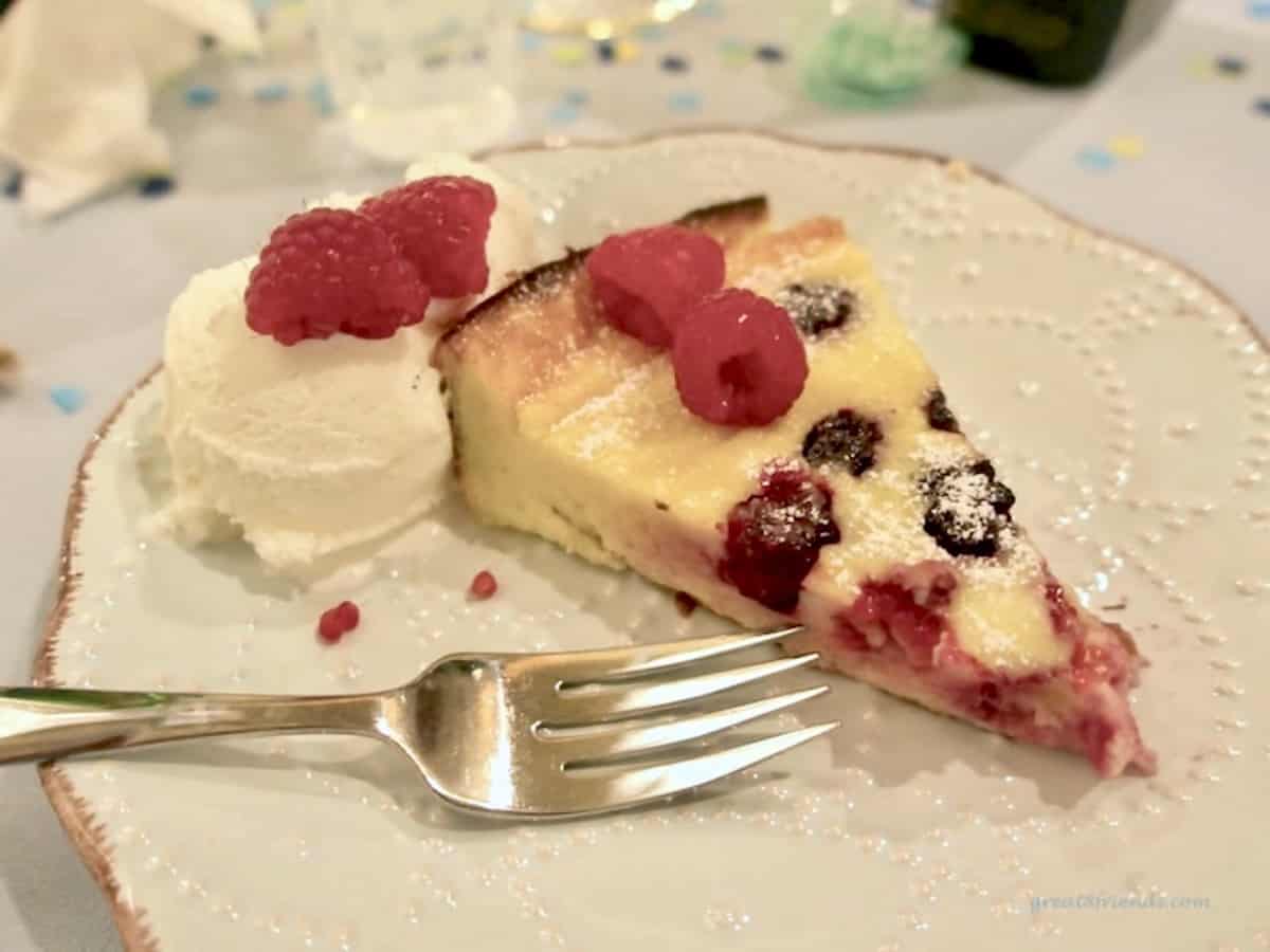 A slice of a berry dutch baby pancake on a white plate served with vanilla ice cream and fresh raspberries.