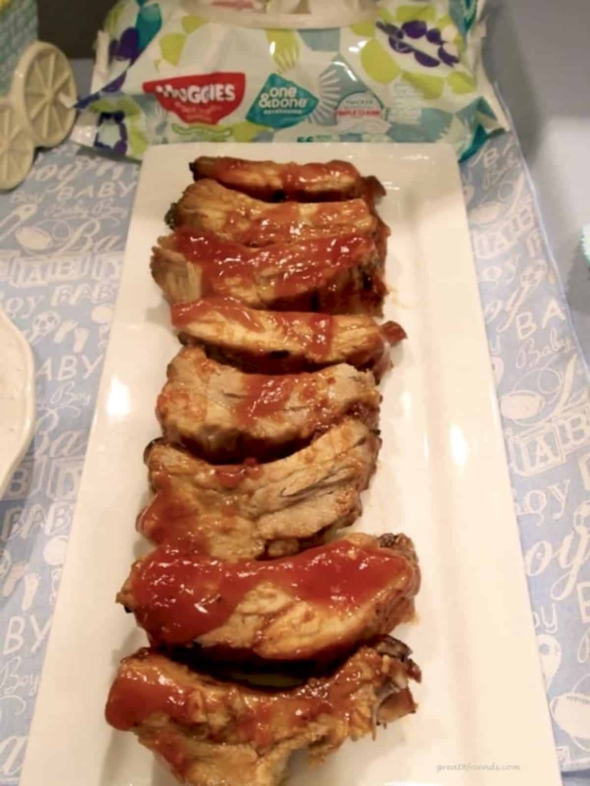 Baby back ribs served on a white rectangular platter with barbecue sauce on top.