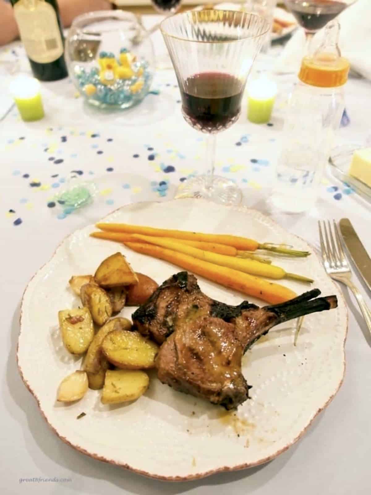 Dinner table with a place setting of lamb chops, roasted potatoes and carrots.