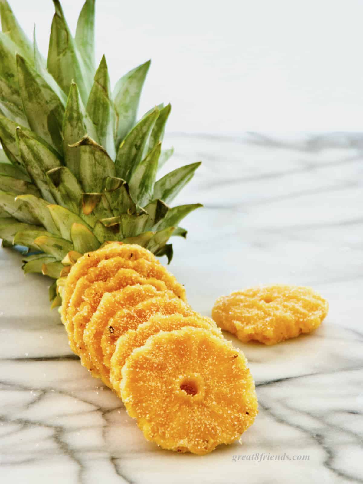 Candied pineapple slices lined up with a pineapple top at the back.