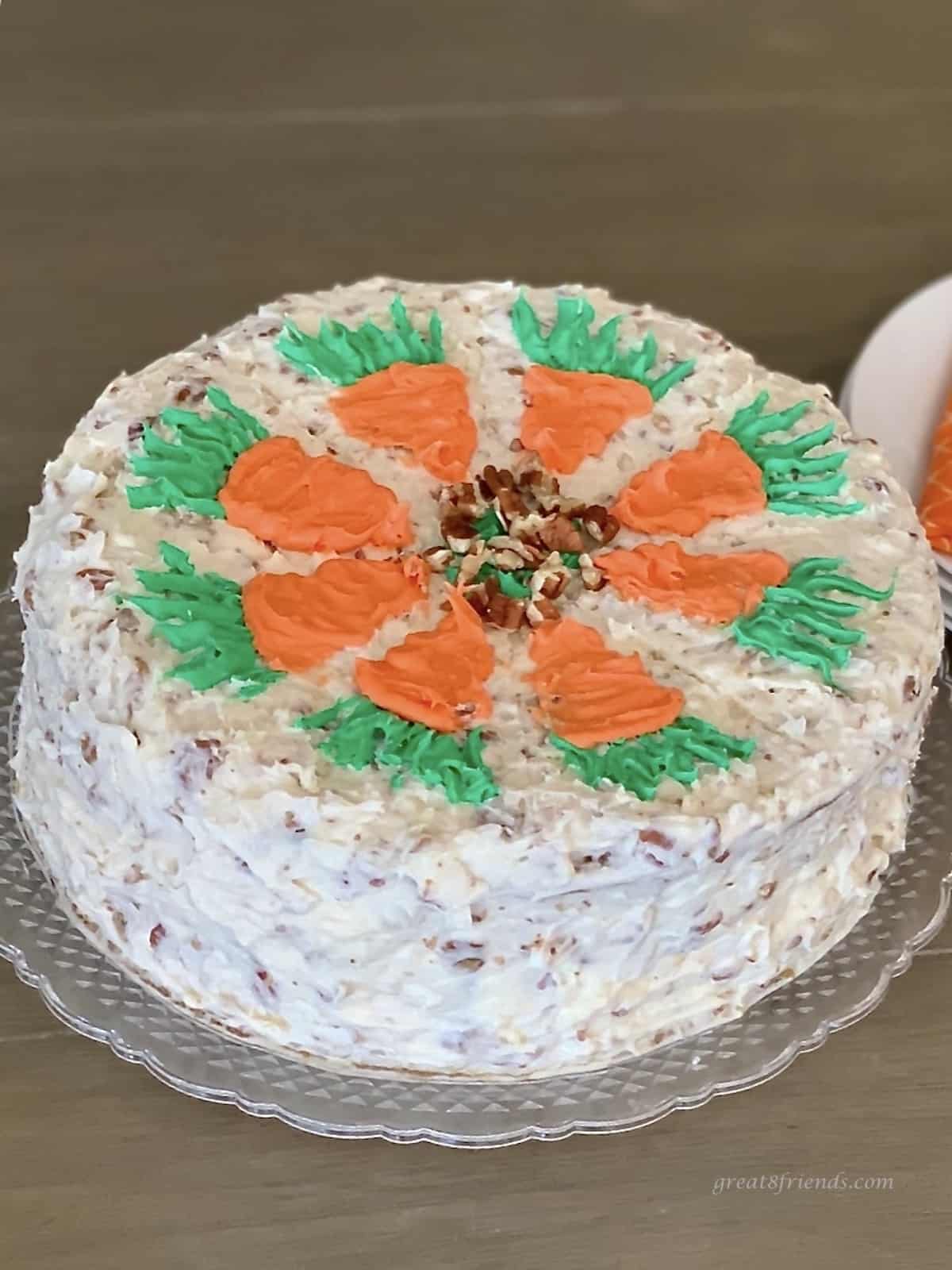 Two layer round carrot cake with pecan cream cheese frosting with pecans and decorated with icing carrots on the top.