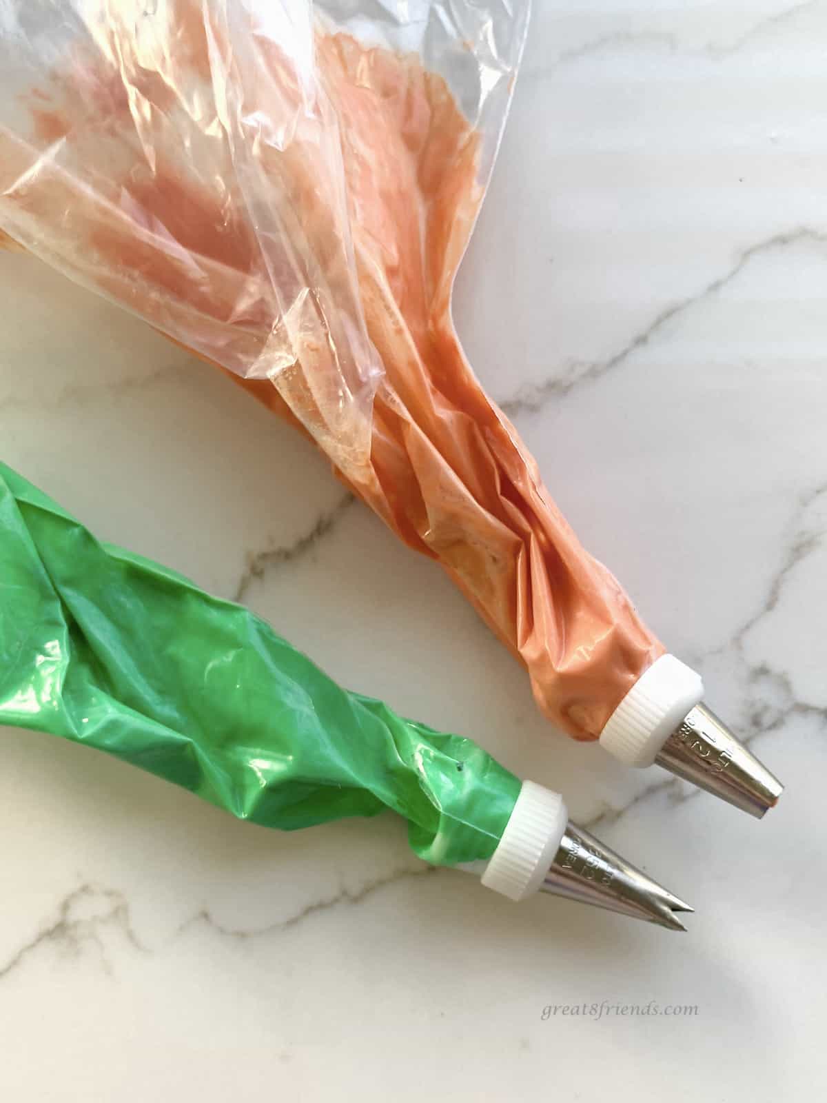 Two plastic bags with decorator tips with orange and green icing in the bags.