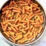 A large round pan of baby carrots sprinkled with orange segments.