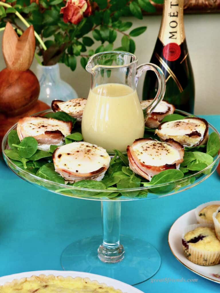 Glass pedestal with eggs benedict muffin cups and a glass pitcher of hollandaise in the center.