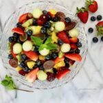Overhead shot of fruit salad in a glass bowl on a marble slab.