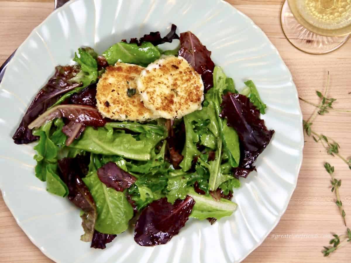 Green and red lettuce on a light blue plate with two fried goat cheese rounds on top.