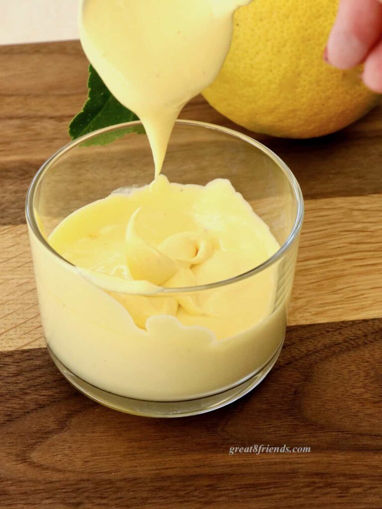 Hollandaise sauce being dripped from a spoon into a glass dish.