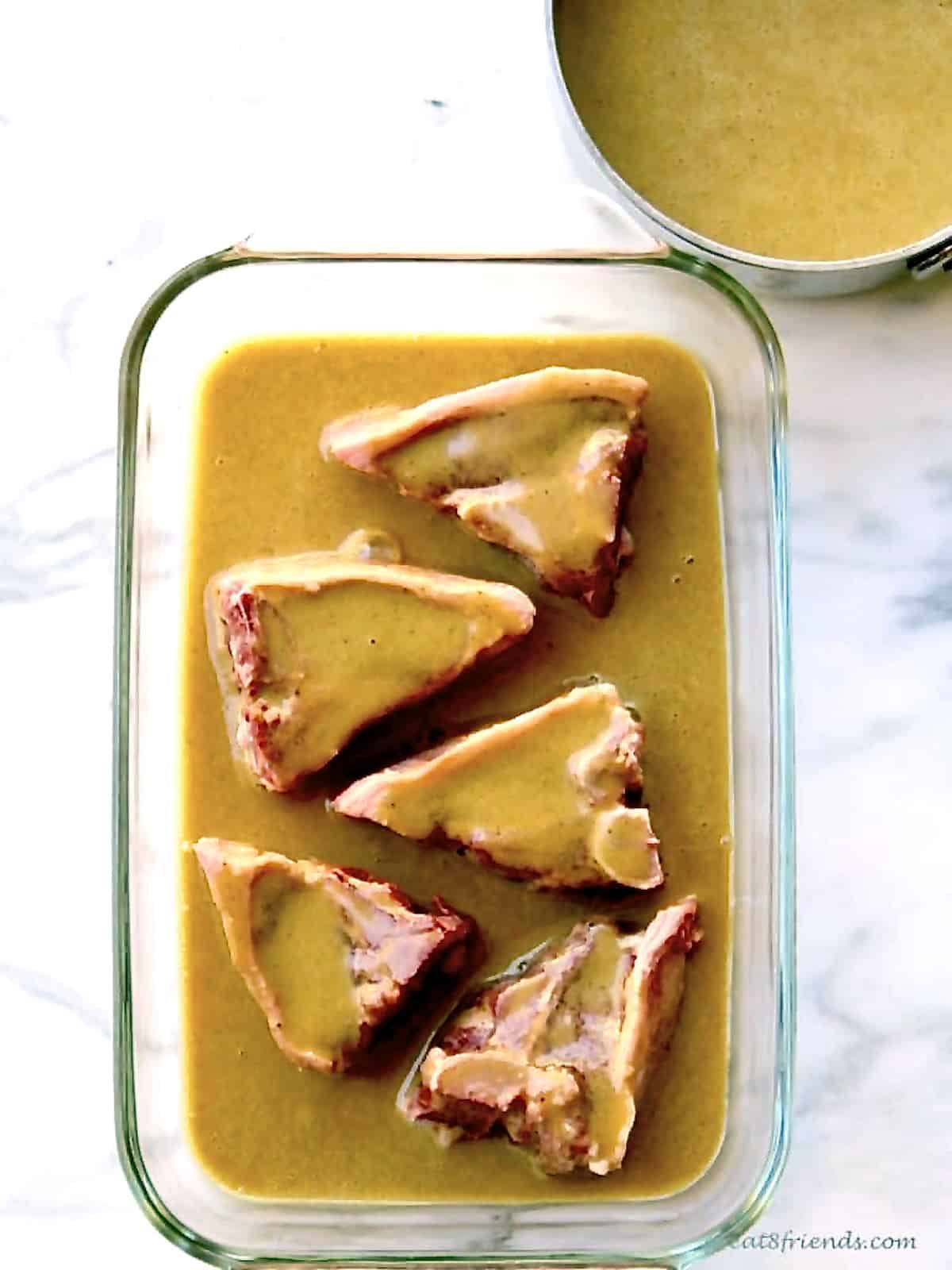 Four lamb chops marinading in a large glass oblong dish with a pan of marinade on the side.