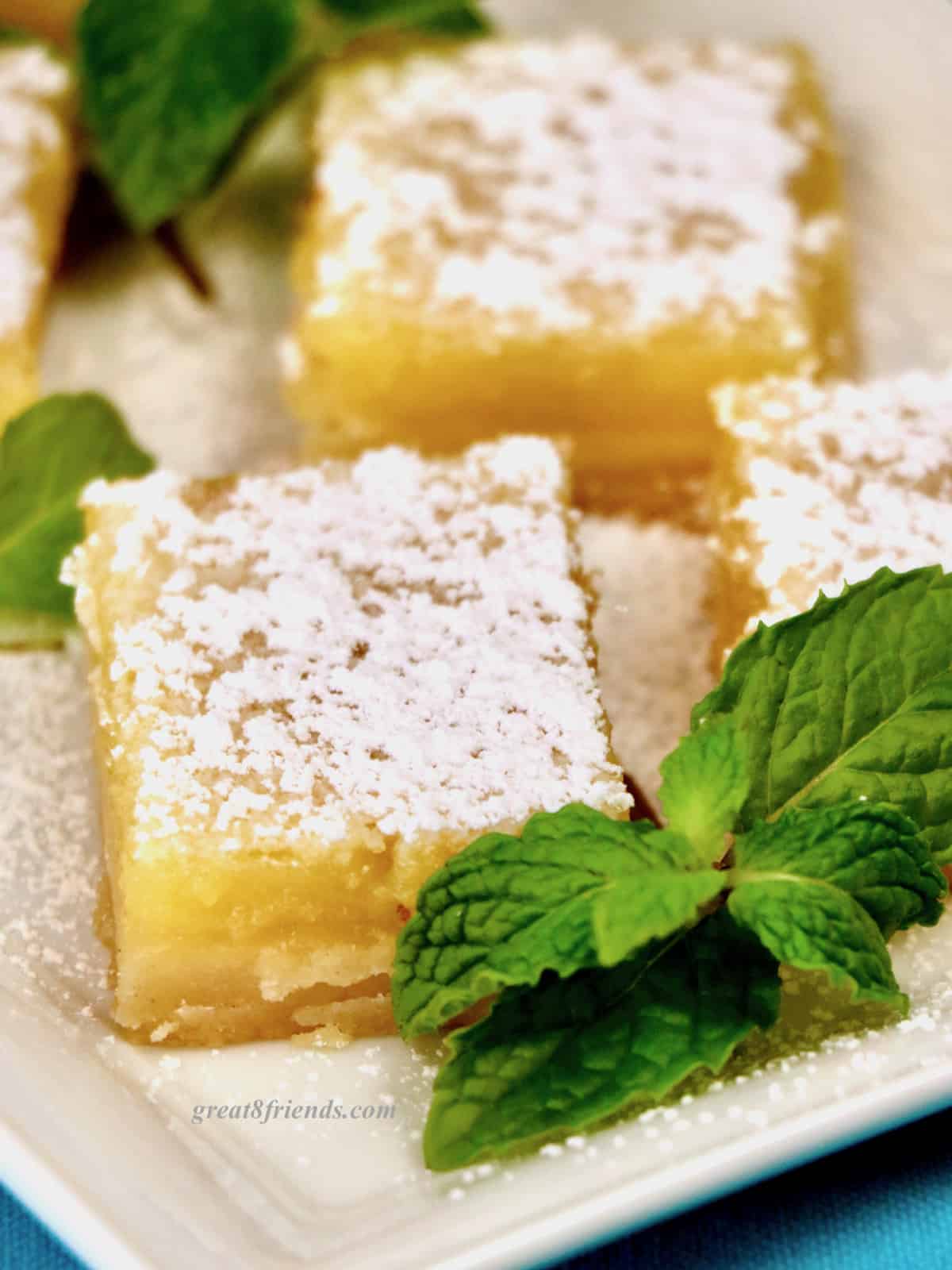 Close up of lemon bars topped with powdered sugar and garnished with a sprig of mint.