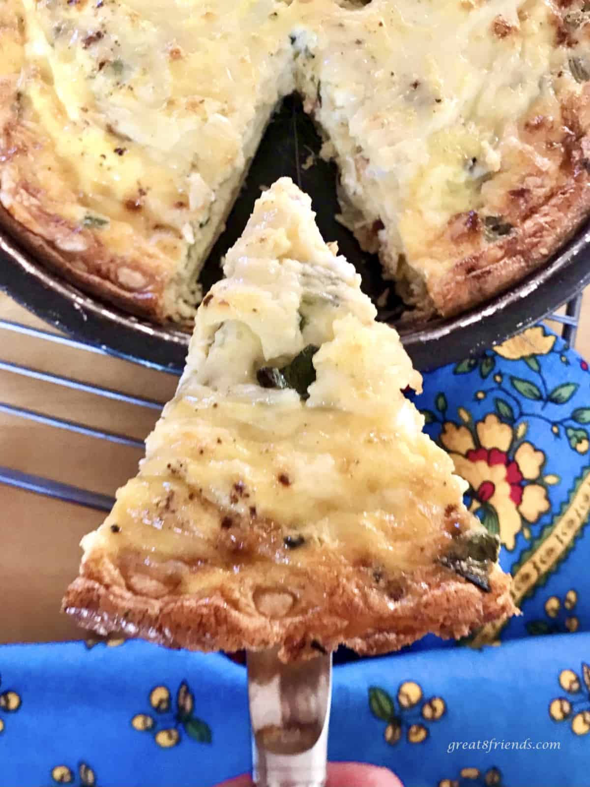 A piece of quiche on a spatula being held over the quiche Lorraine in the pie dish.