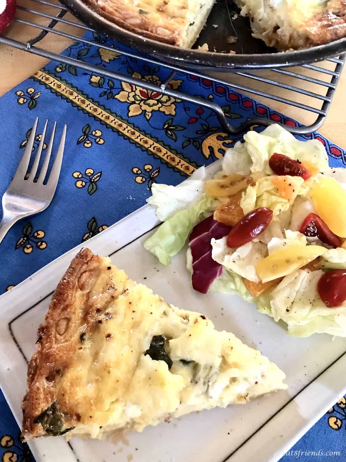 A slice of quiche on a plate with a small side salad.