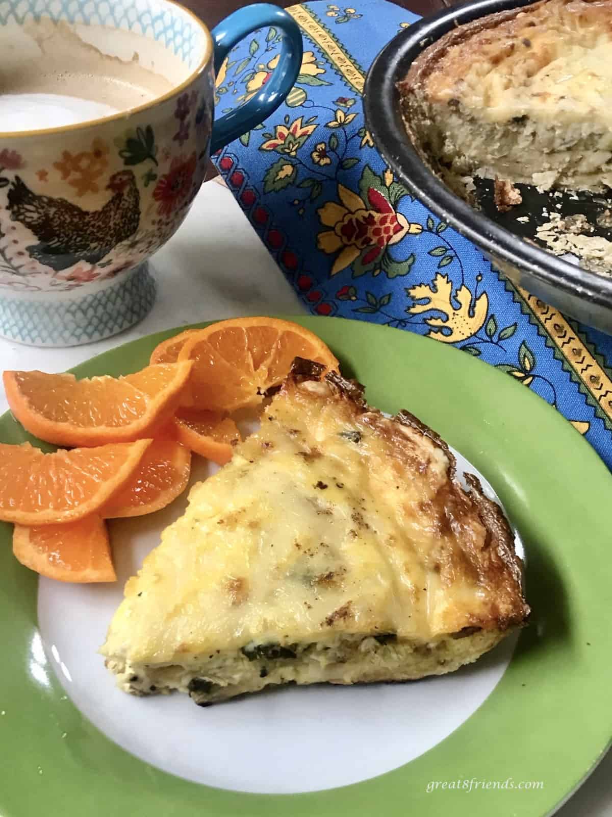 A slice of quiche lorraine on a white and green plate with orange slices and a cappuccino on the side.