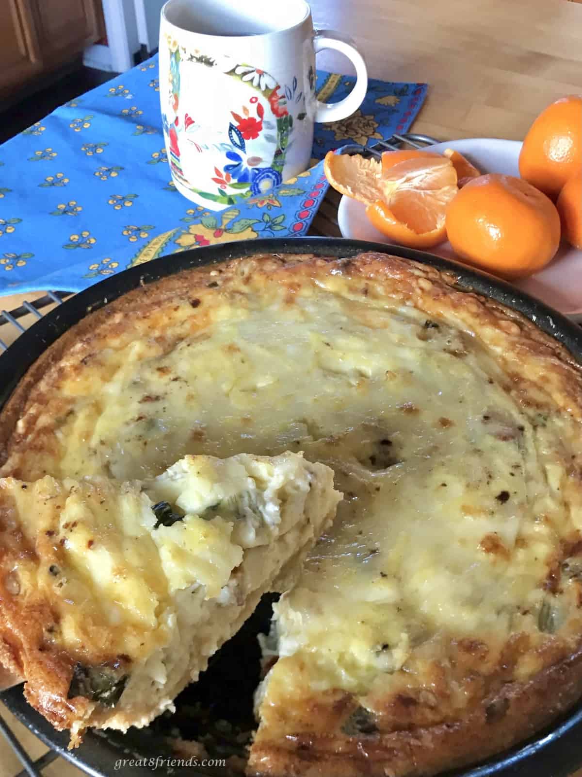 A Quiche Lorraine egg pie with a one piece being sliced with tangerines and coffee on the side.