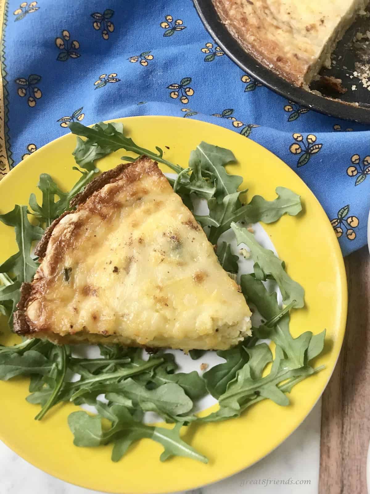 A slice of a Quiche Lorraine served on a bed of arugula on a bright yellow plate.