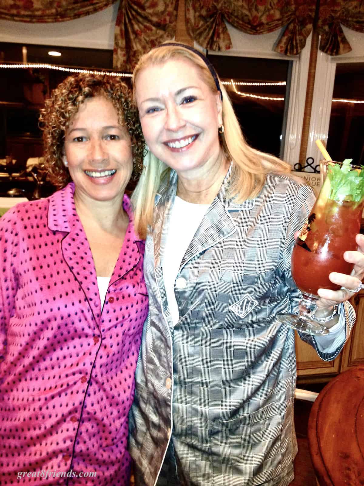 Two women posing for the camera one has a tall glass with a Bloody Mary in it.