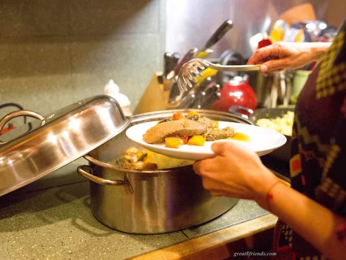 Cooked Brisket and vegetables being served onto a plate from a large stainless pan.