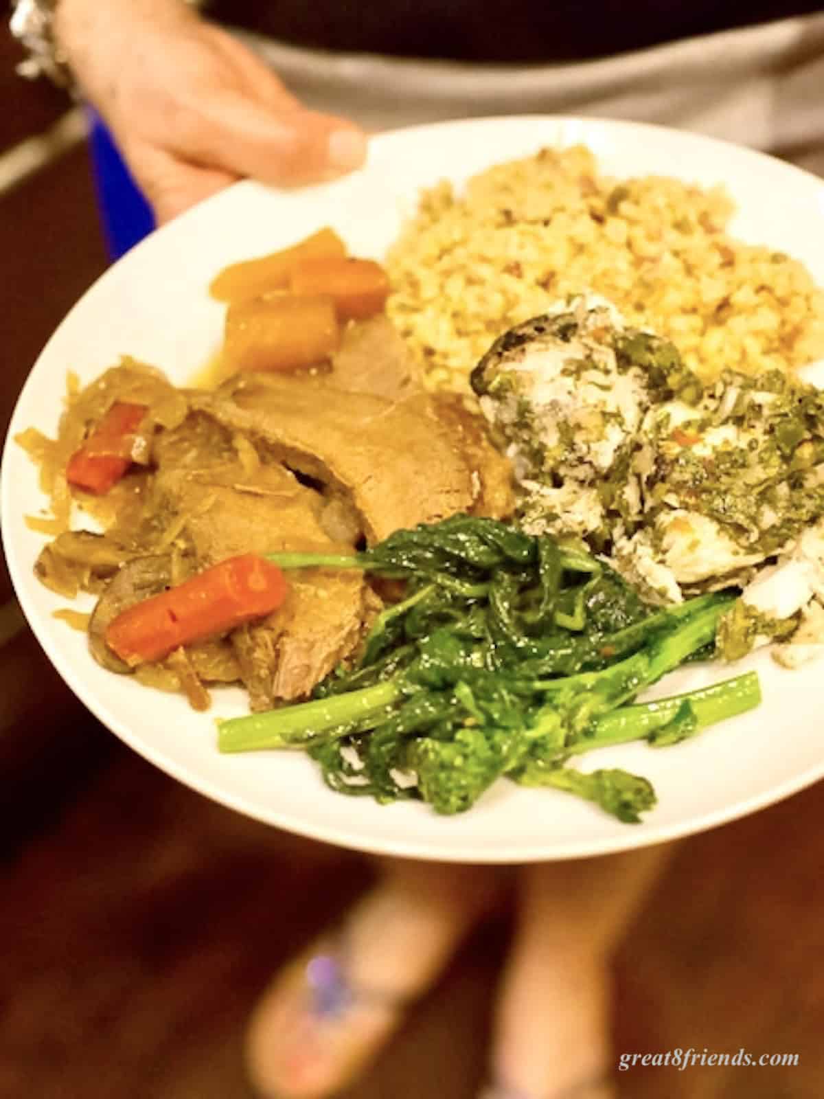 Someone is holding a plate with brisket, broccoli rabe, fried corn and chicken on it.