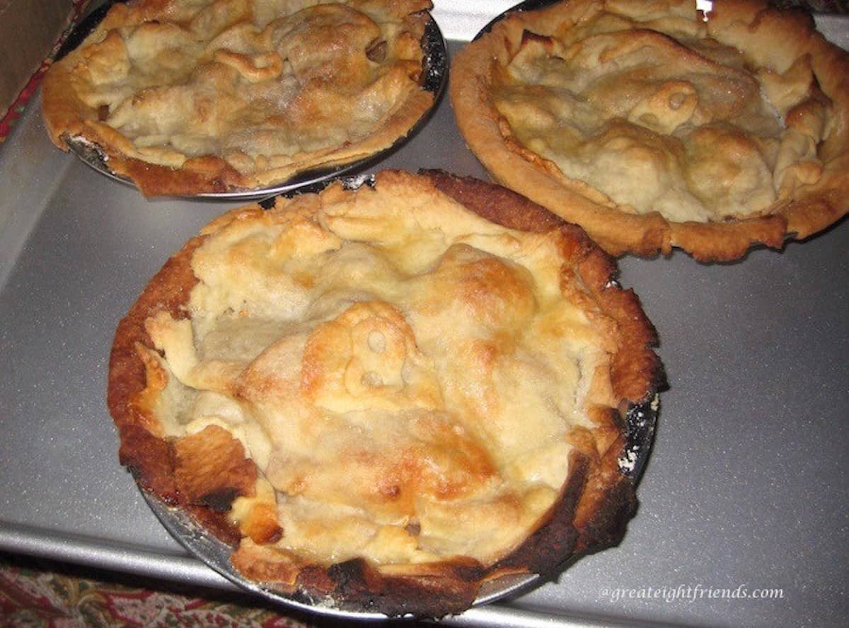 Three individual apple pies on a baking sheet.