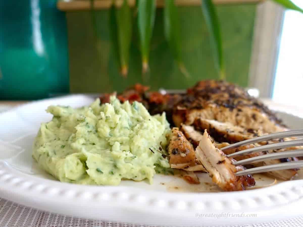 A white dinner plate with basil pureed potatoes and roasted chicken on it.