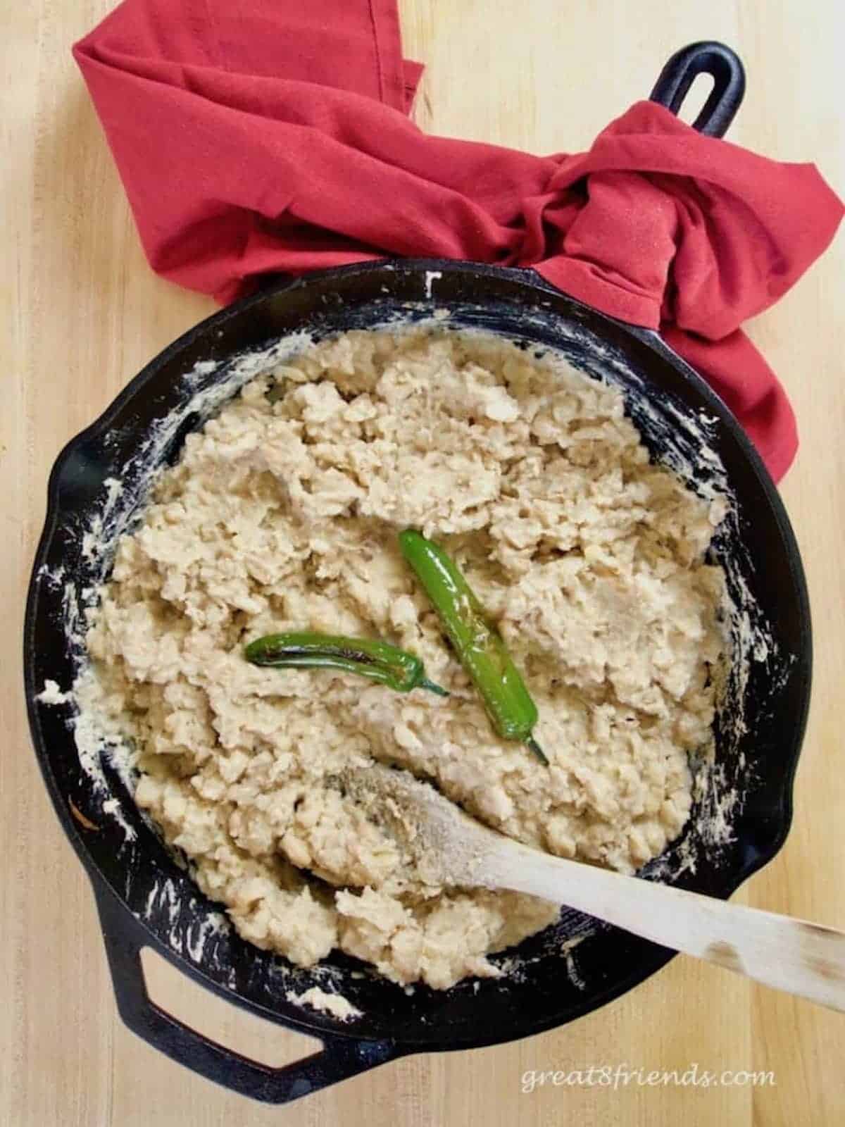 Refried beans in a black cast iron skillet with two whole jalapeños on top and the handle of the skillet wrapped with a red cloth napkin.