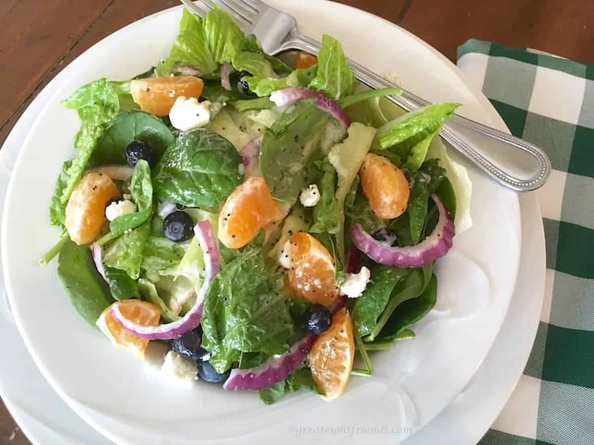 Spinach, orange, red onion salad served with a poppyseed dressing on a white plate.