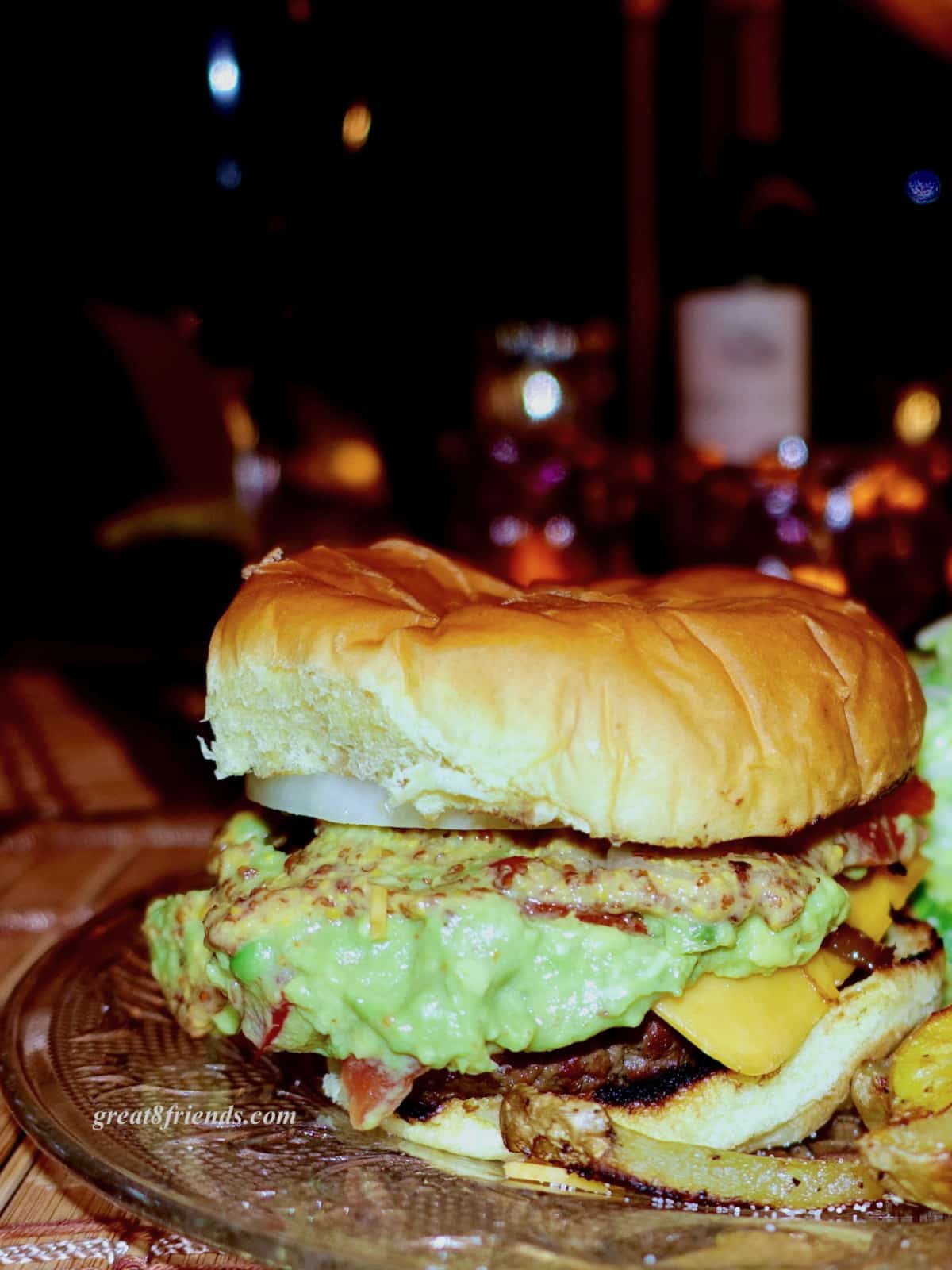 Grilled hamburger on a bun with cheese, mustard and guacamole.