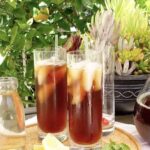 Two glasses of iced tea on a tray with some lemon wedges and mint leaves.