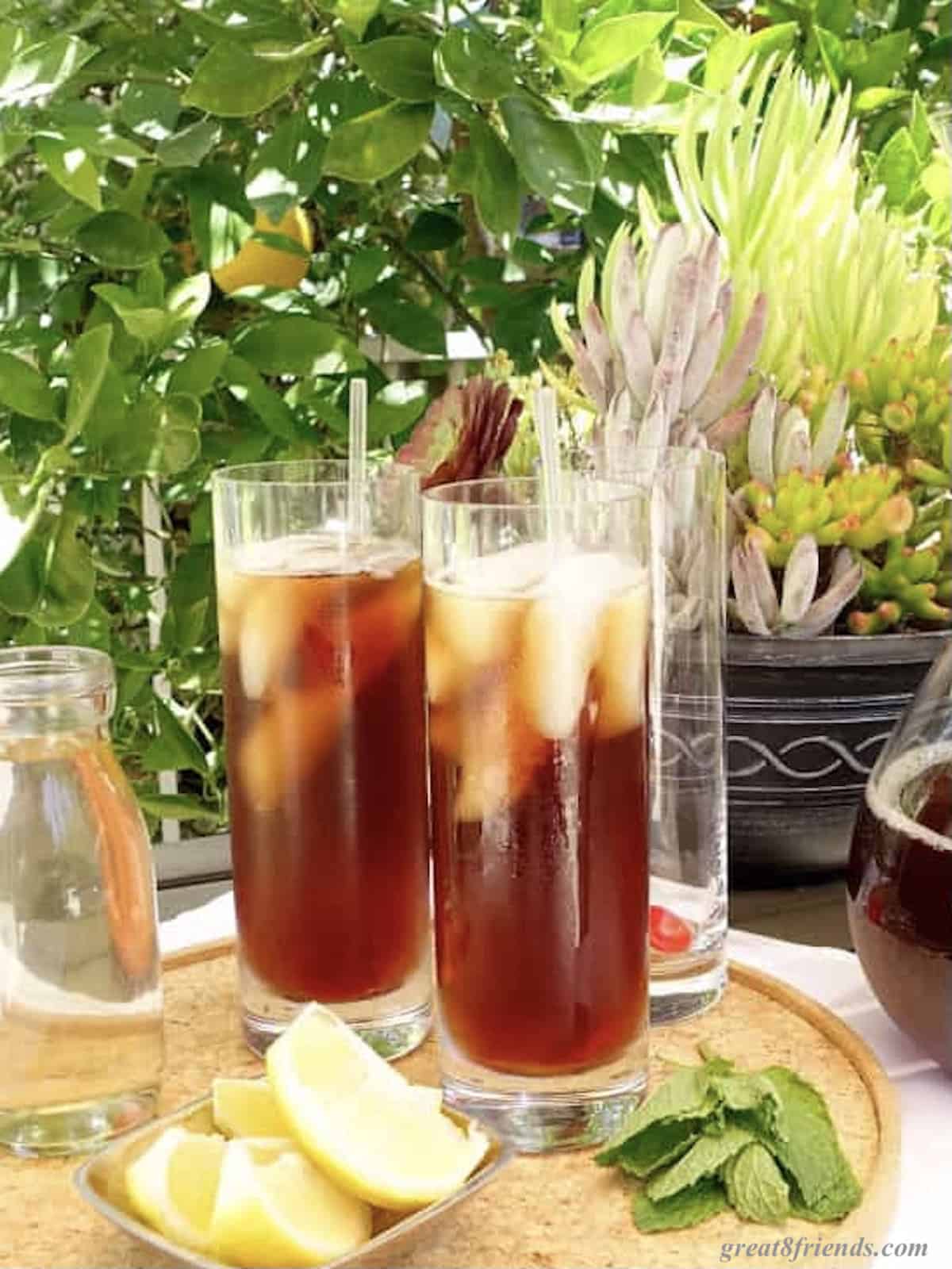 Two glasses of iced tea on a tray with some lemon wedges and mint leaves.