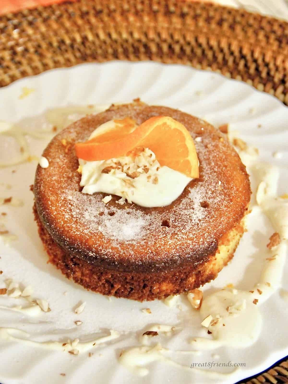 A round cake in the middle of a white plate with whipped cream and an orange slice on top.