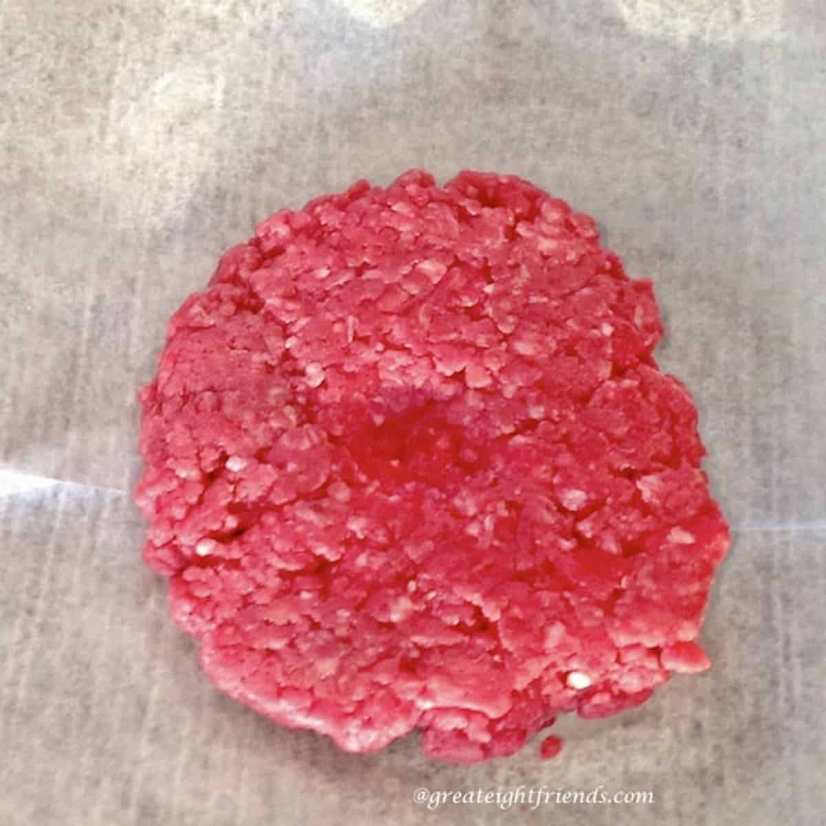 Raw hamburger with a dimple pressed in the middle of it.